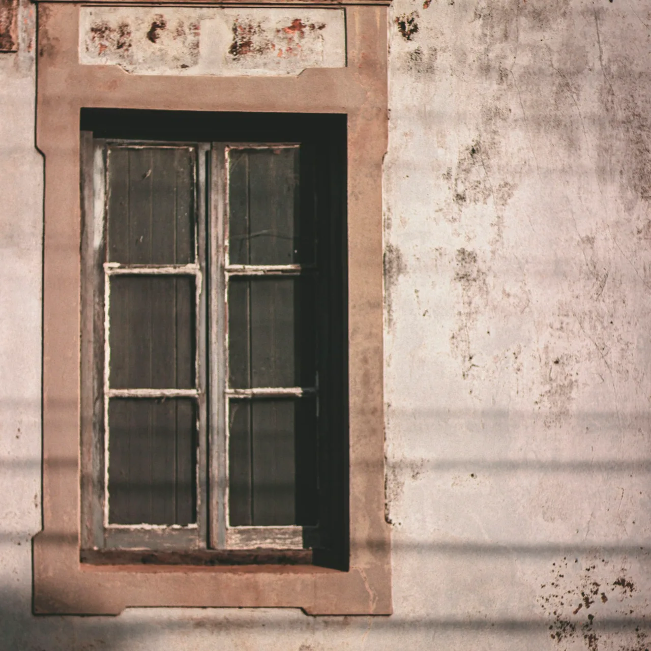 Six-pane window against a worn monochrome wall.